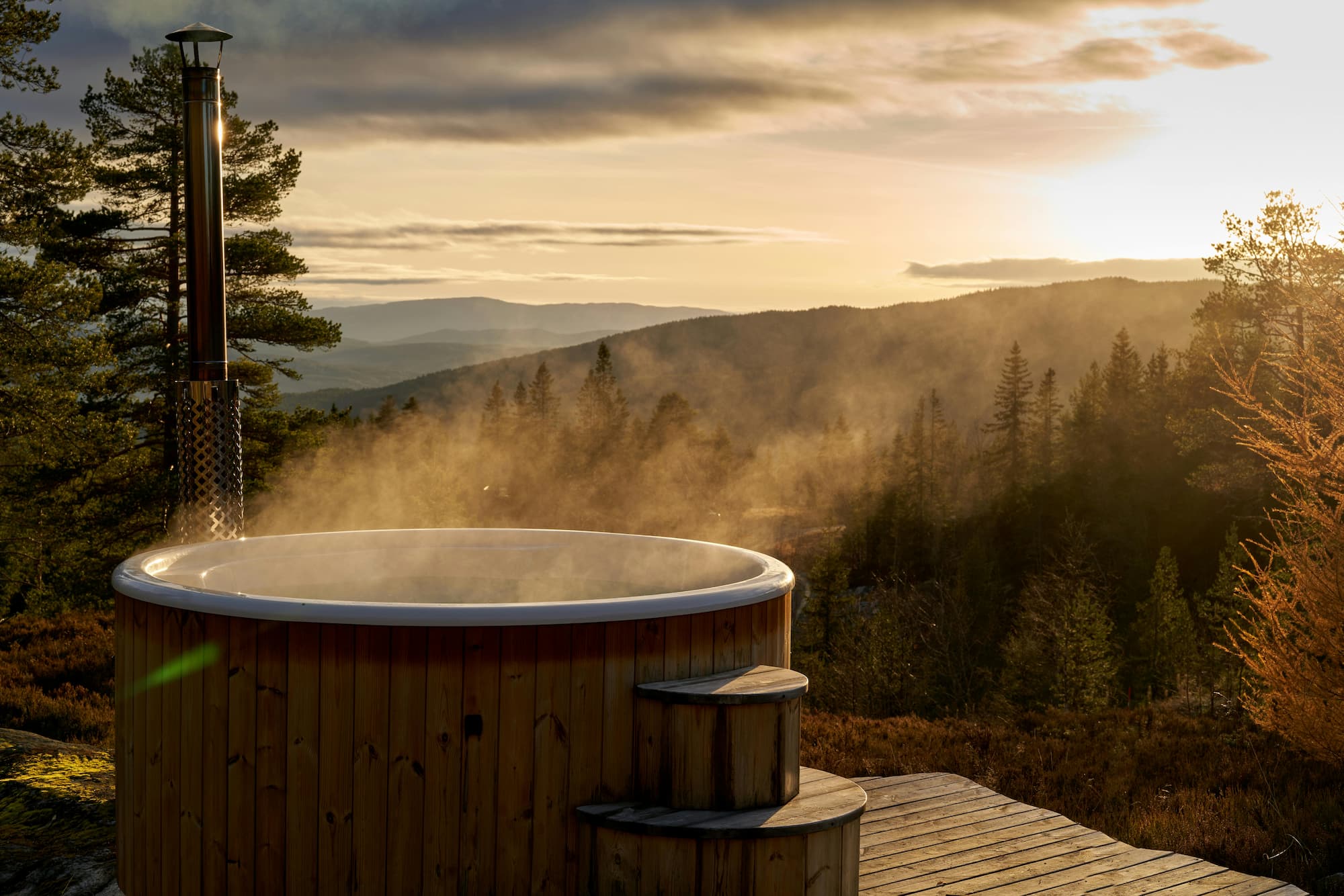 wood fired hot tub with steam rising overlooking mountains at sunset in a natural outdoor setting